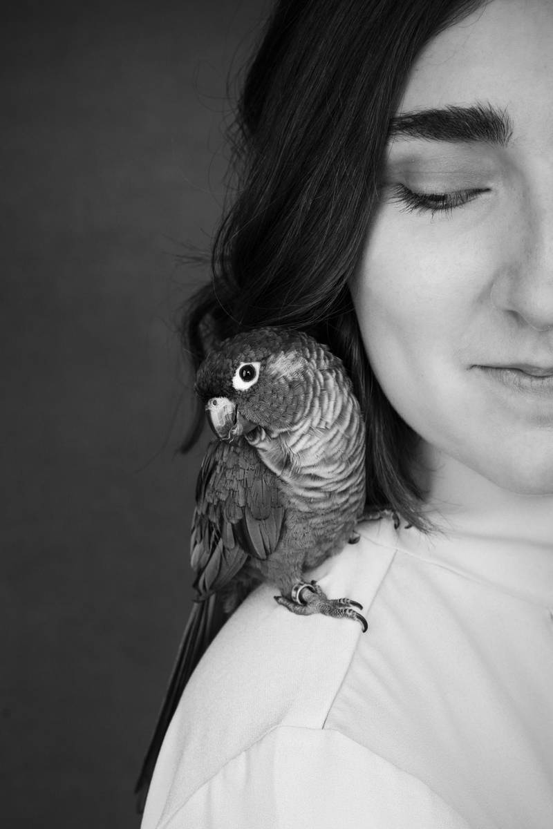 Parrot sitting on a shoulder of beautiful school gir in black and white colors