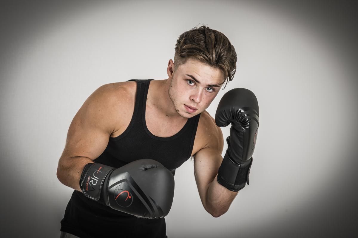 a guy with dark hair and in a black t-shirt in black boxing gloves aura sports ready to fight