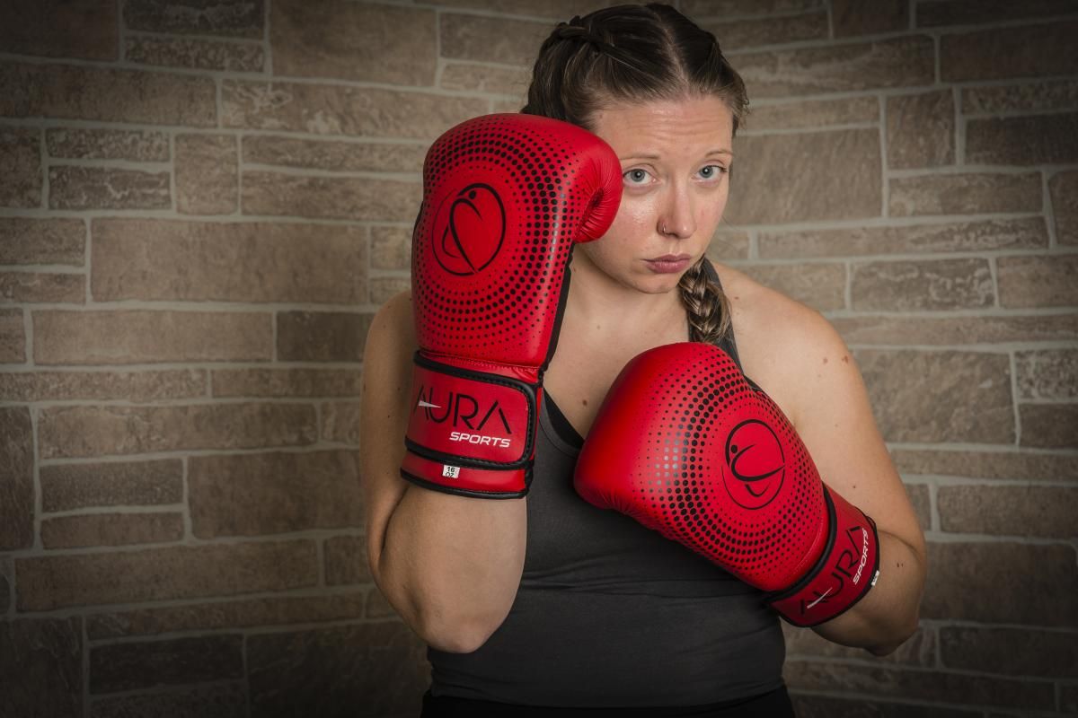 a girl in a dark gray sports top and boxing red gloves aura sports posing full face