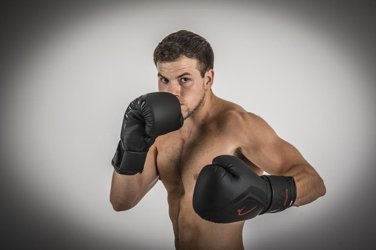 bare chested boxer in defense position wearing black boxing gloves aura sports