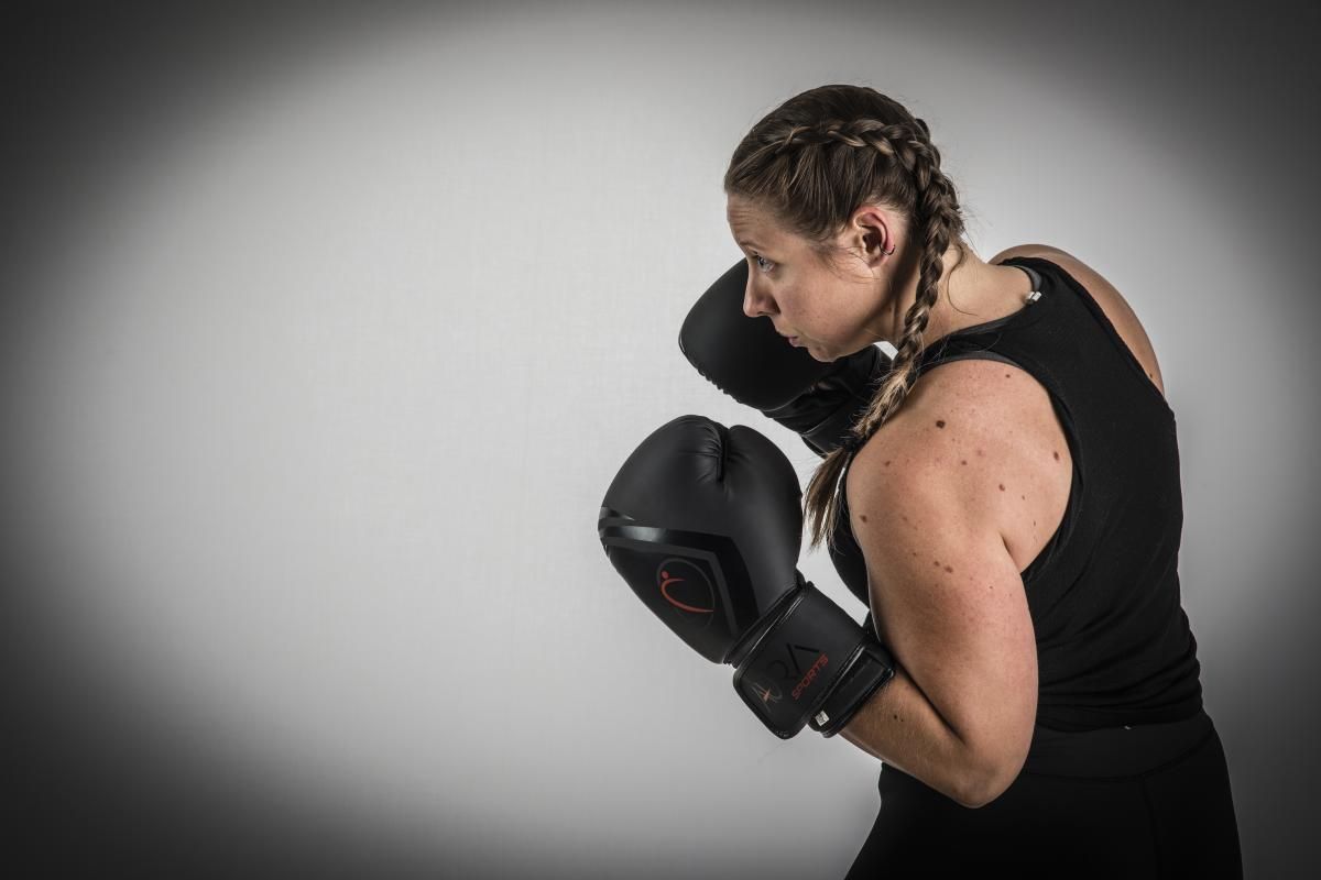 girl in a black sports top with braided hair and boxing black gloves aura sports posing in profile