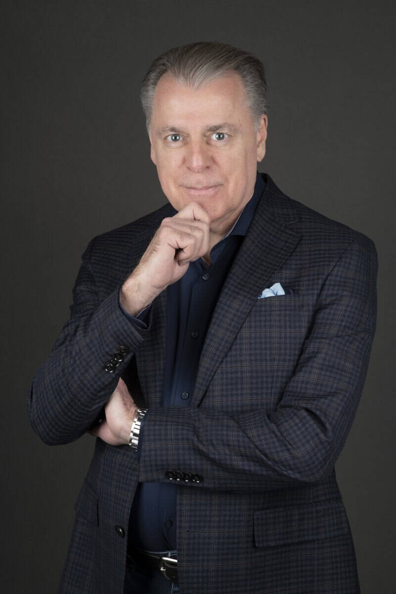 Middle-aged professional man in a navy plaid blazer and blue dress shirt posing for an executive headshot against a gray background